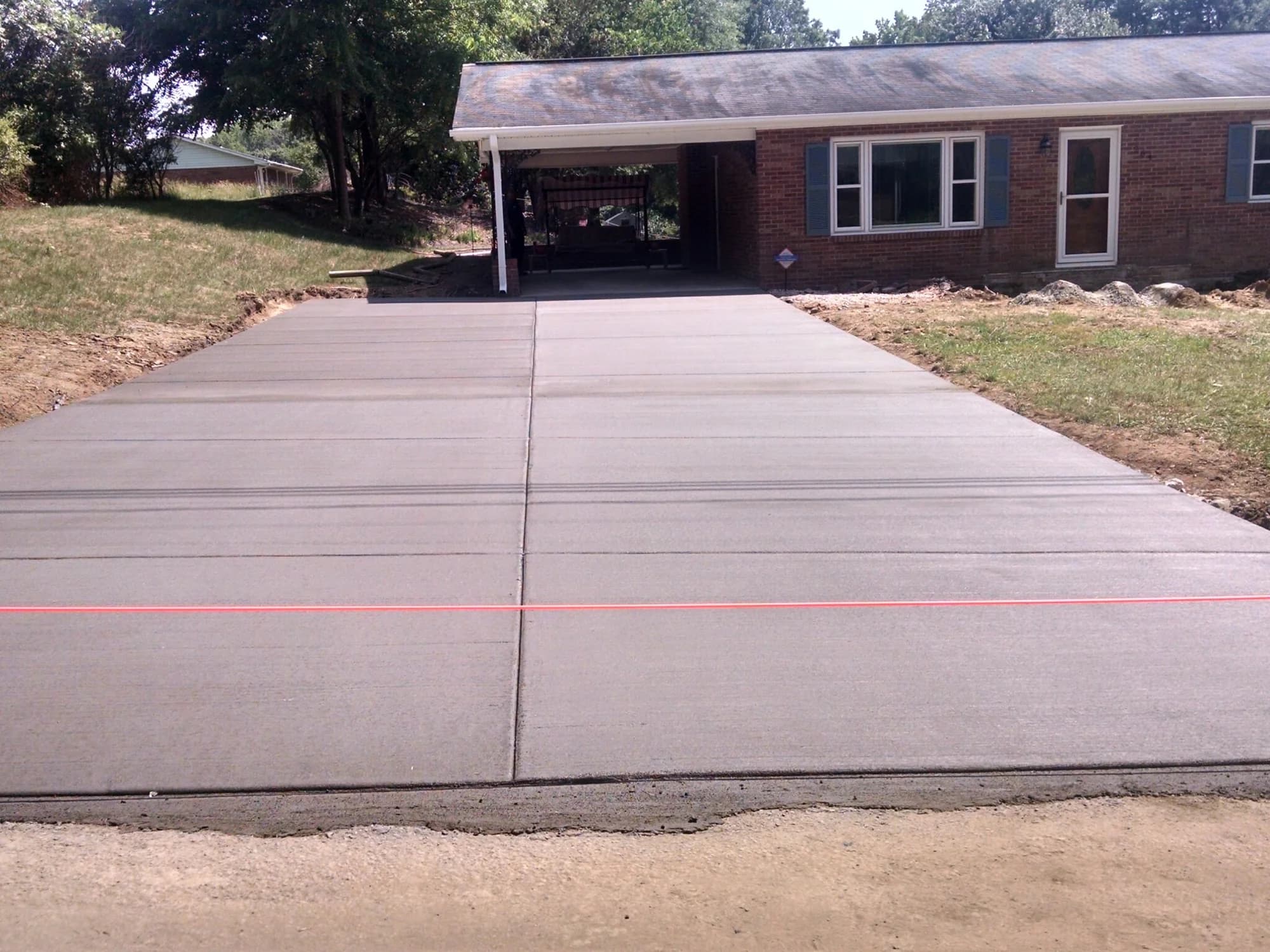 Wide concrete driveway leading to a brick home and carport
