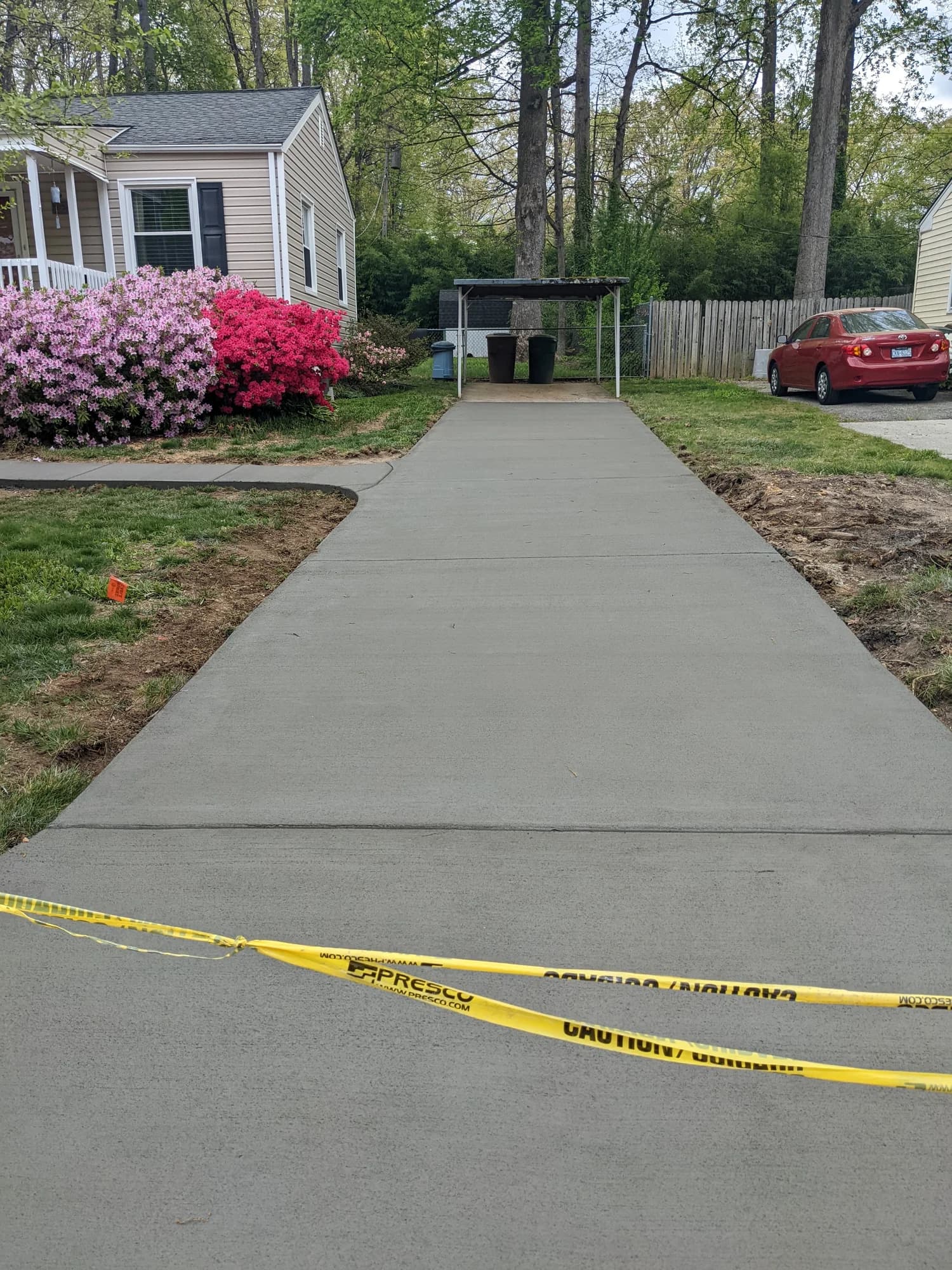 Fresh concrete driveway beside flowering shrubs leading to a covered parking area