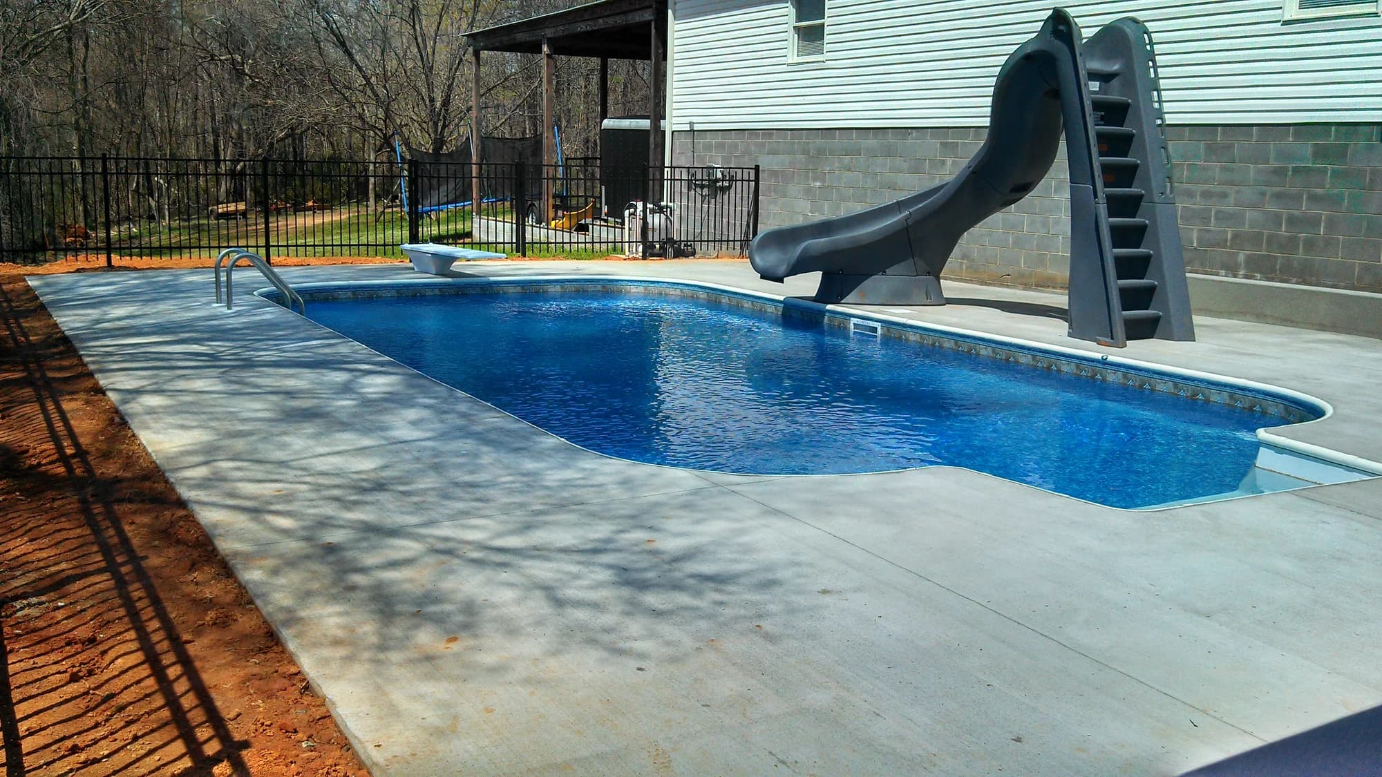Concrete pool deck beside a home with a curved swimming pool and slide