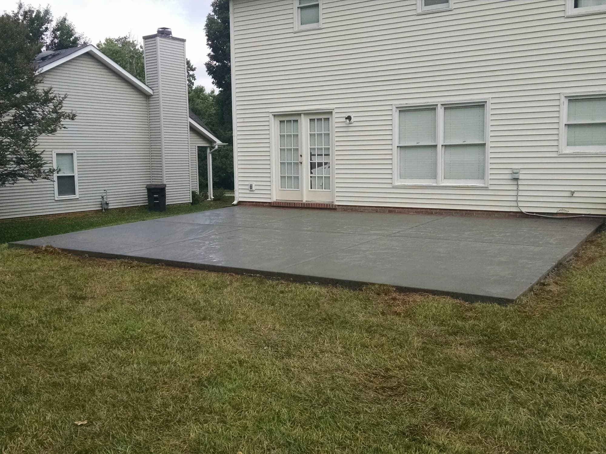 Rectangular concrete patio along the back of a white-sided home