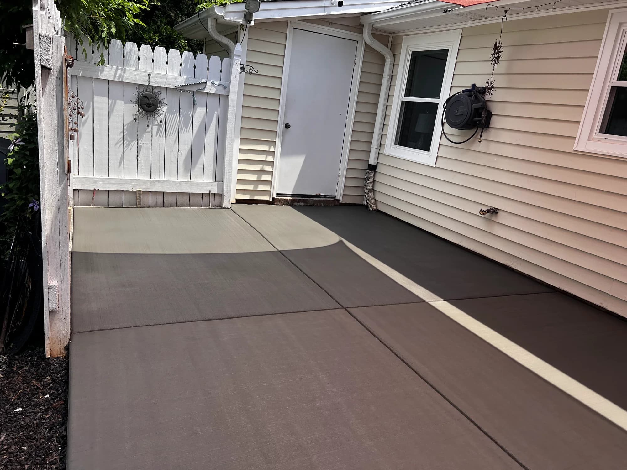 Broom-finished concrete patio beside a home and white garden gate