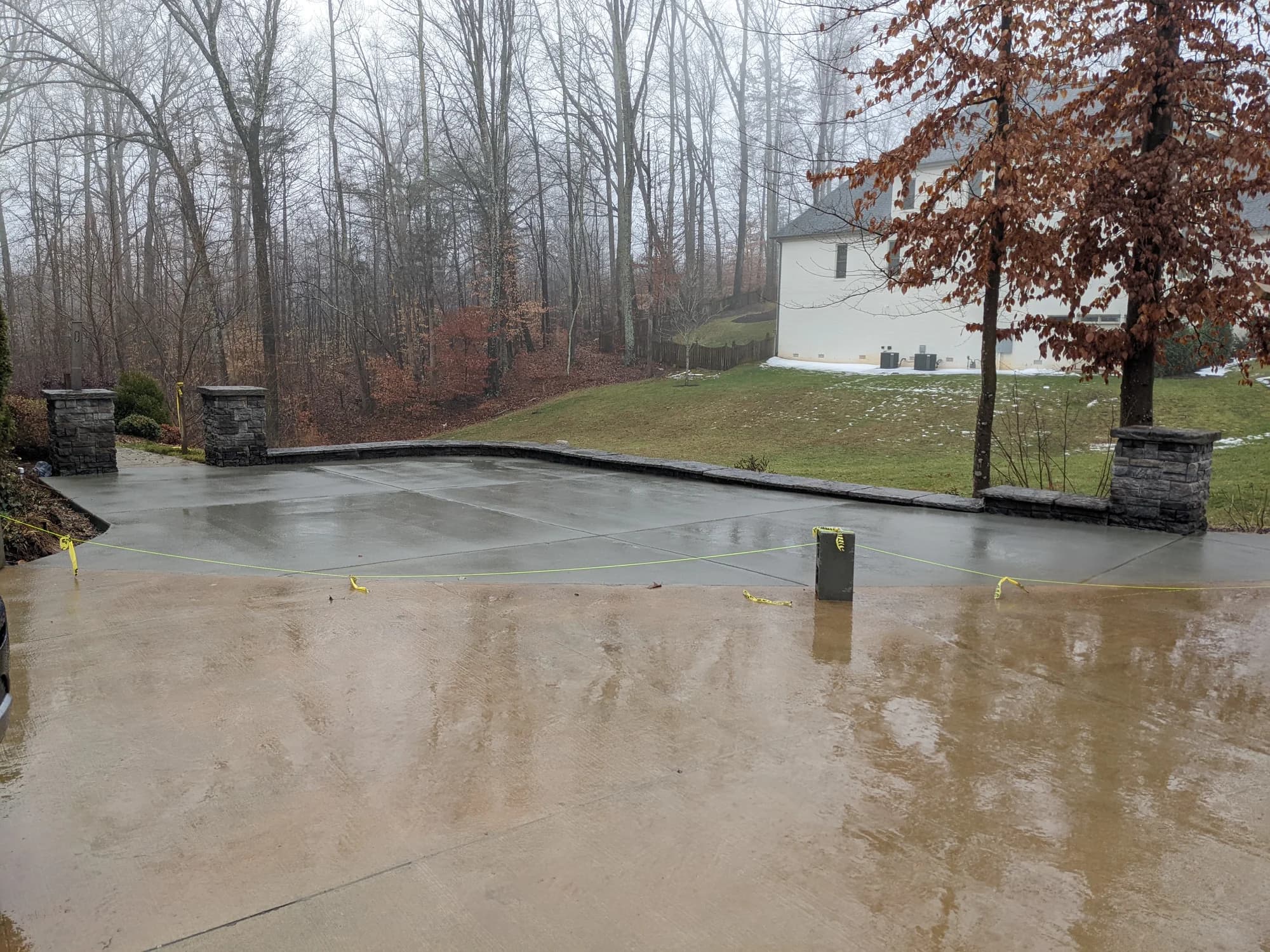 Large concrete patio bordered by stone walls beside a wooded yard