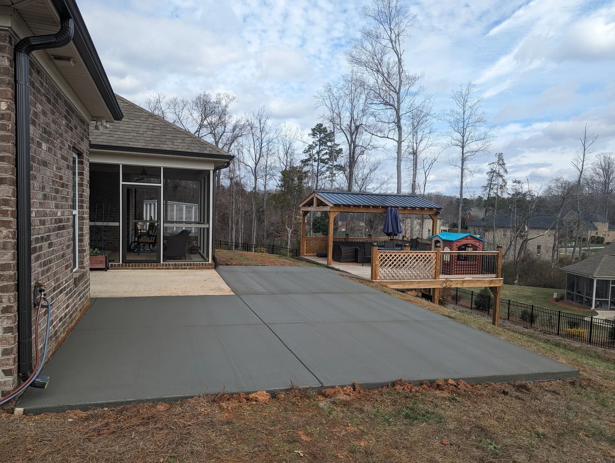 Large rectangular concrete patio beside a brick home overlooking a sloped backyard