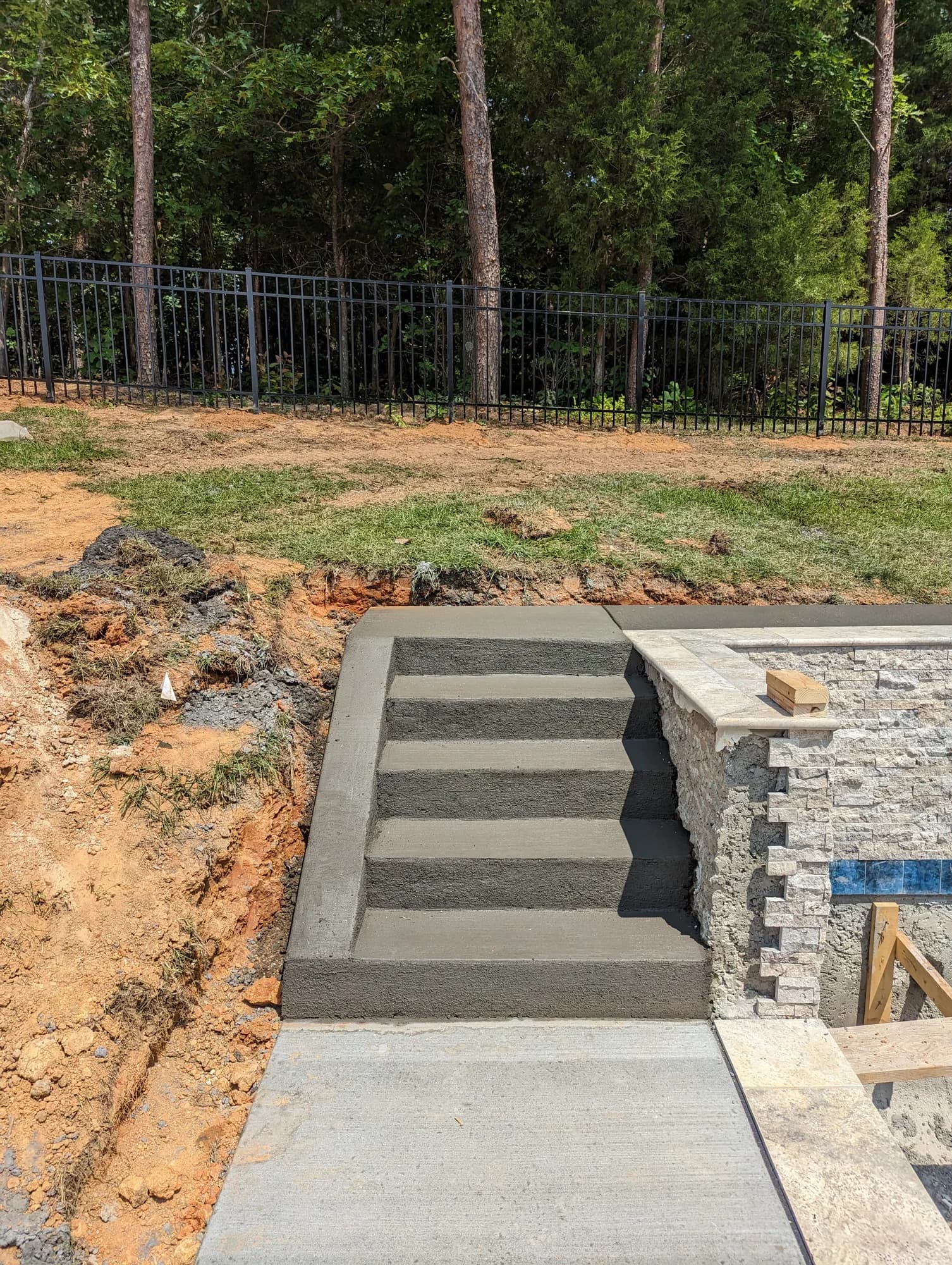 Broom-finished concrete poolside steps beside a stone-faced wall
