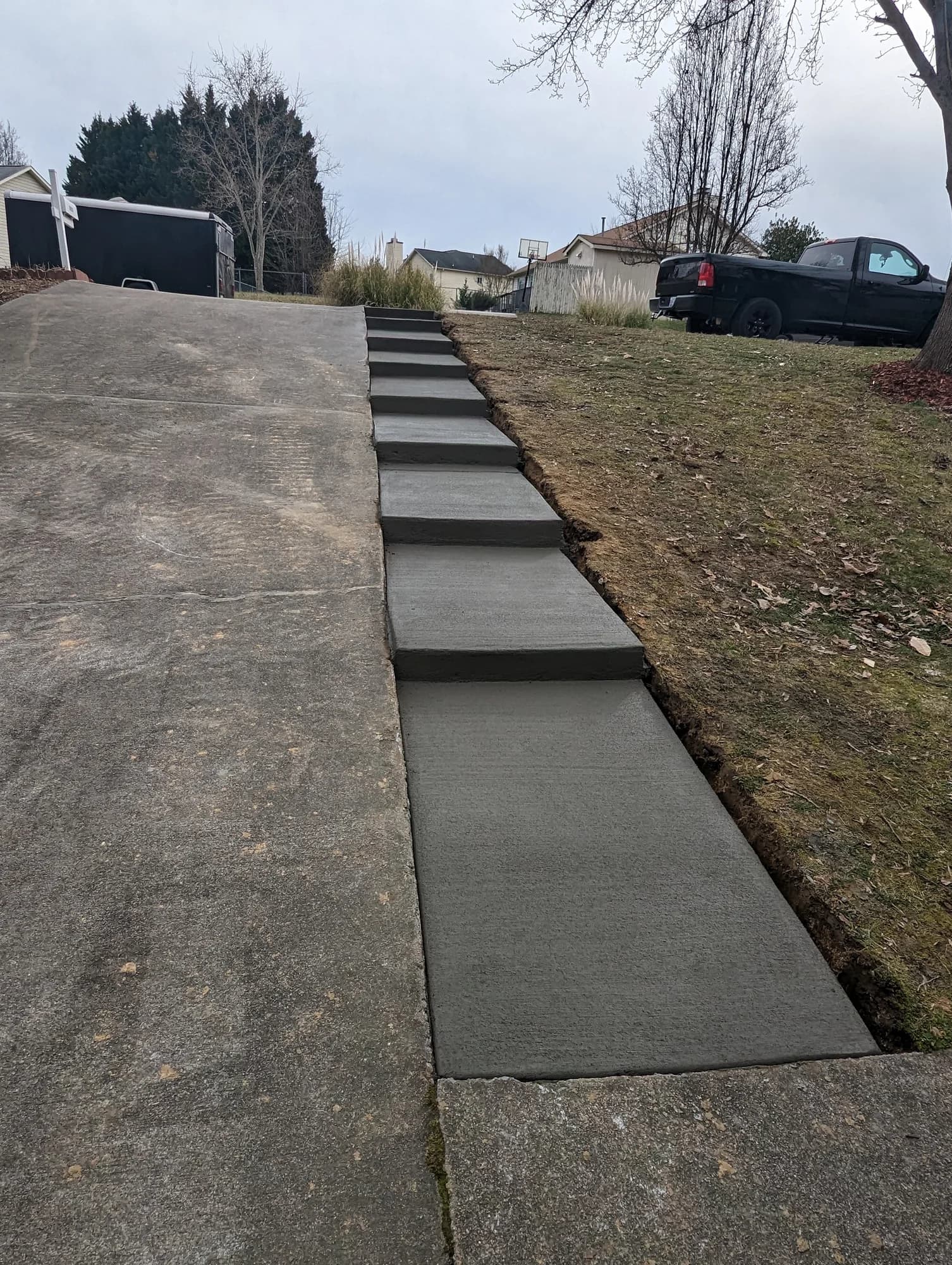 Broom-finished concrete steps climbing a sloped yard alongside an existing driveway