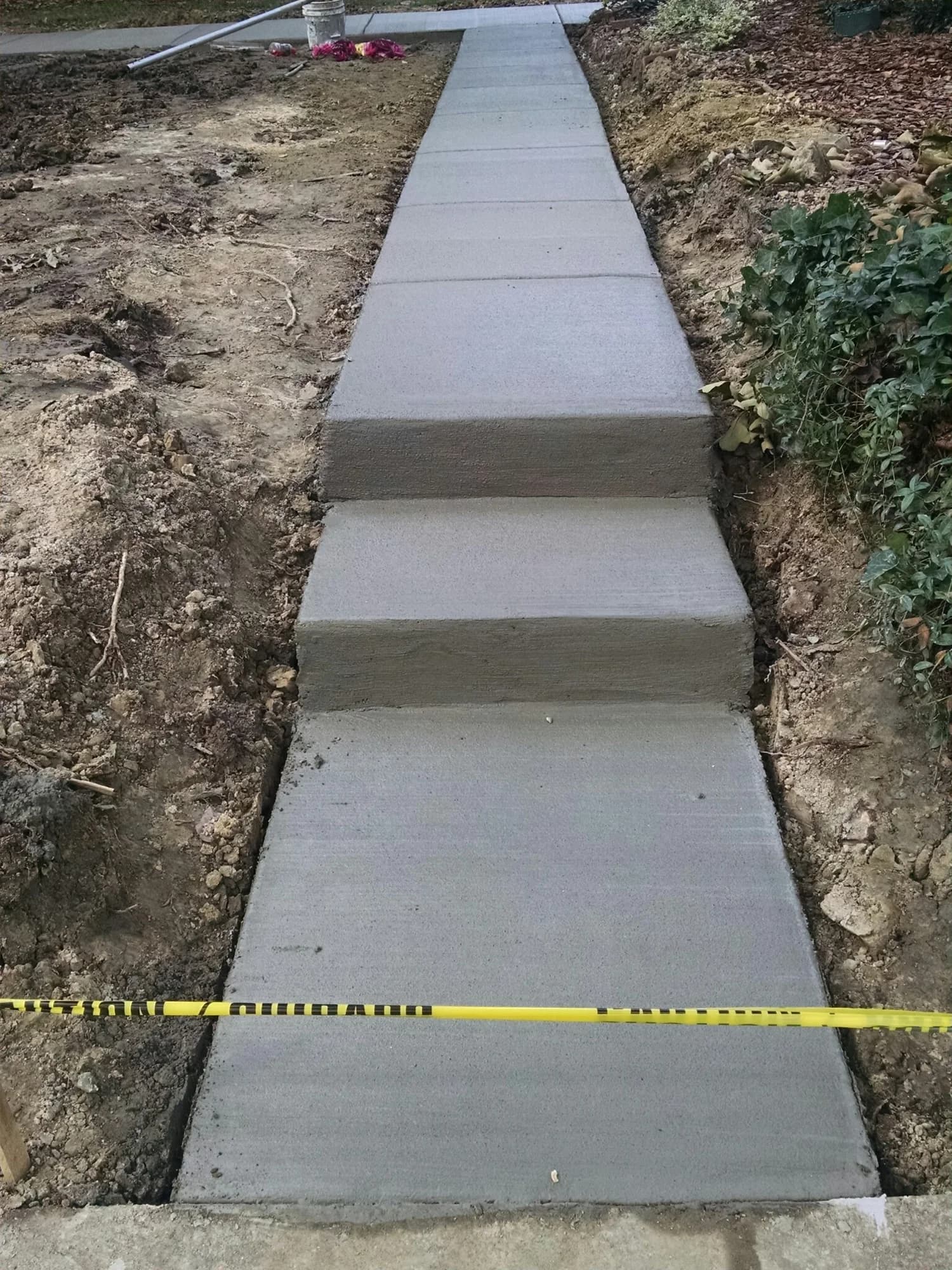 Broom-finished concrete steps connecting a straight walkway through a sloped yard