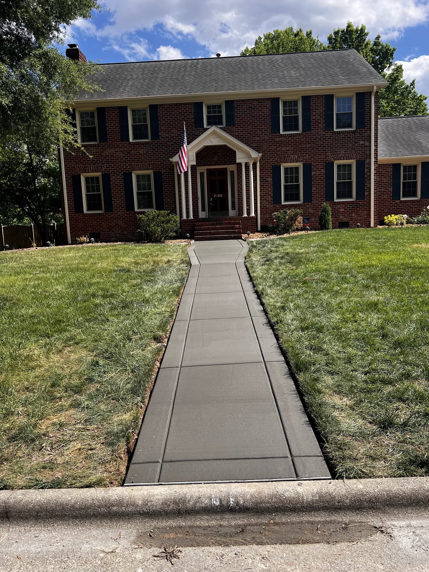 Concrete front walkway with contrasting borders leading to a two-story brick home