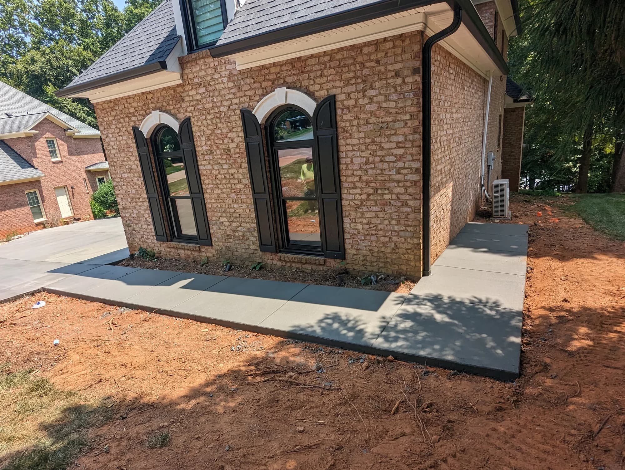 Concrete walkway wrapping around a brick home with tall arched windows