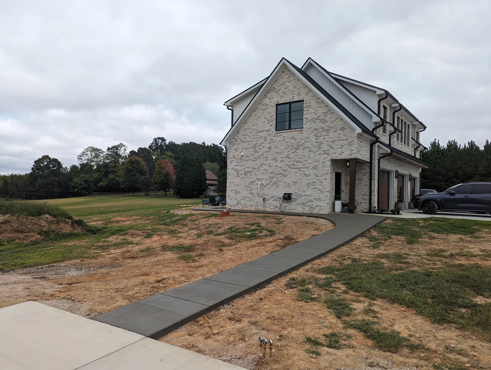 Straight concrete walkway connecting a driveway to a stone-faced home