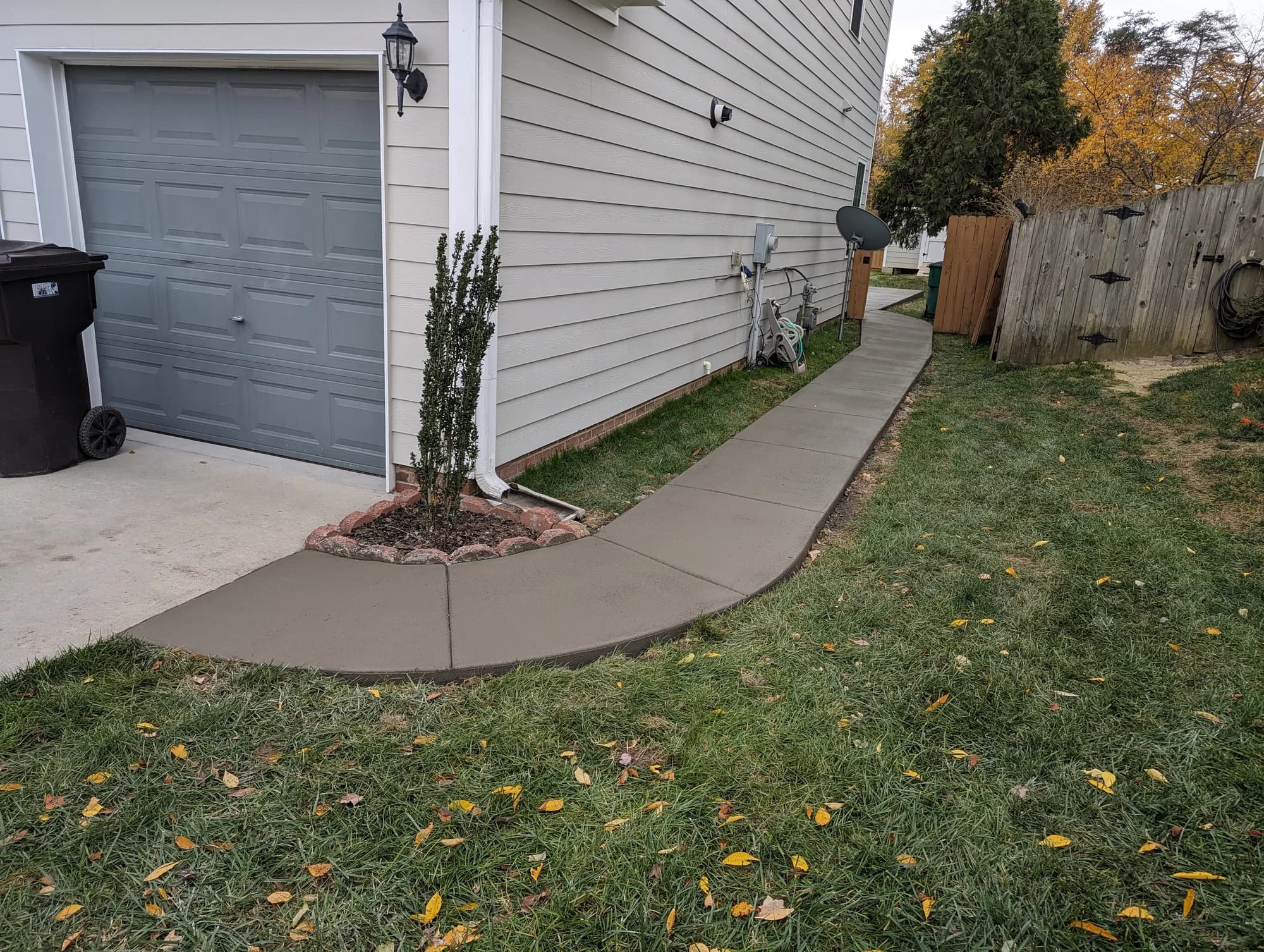 Concrete side walkway curving around a garage toward a fenced backyard