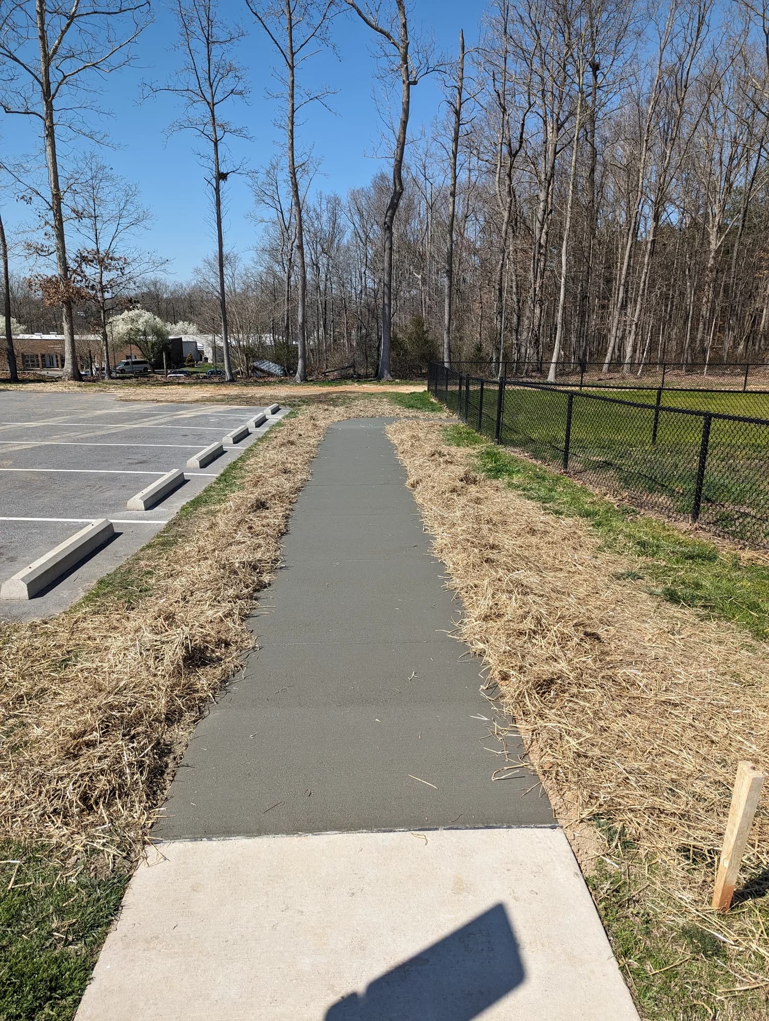 Straight concrete walkway beside a parking lot and black metal fence