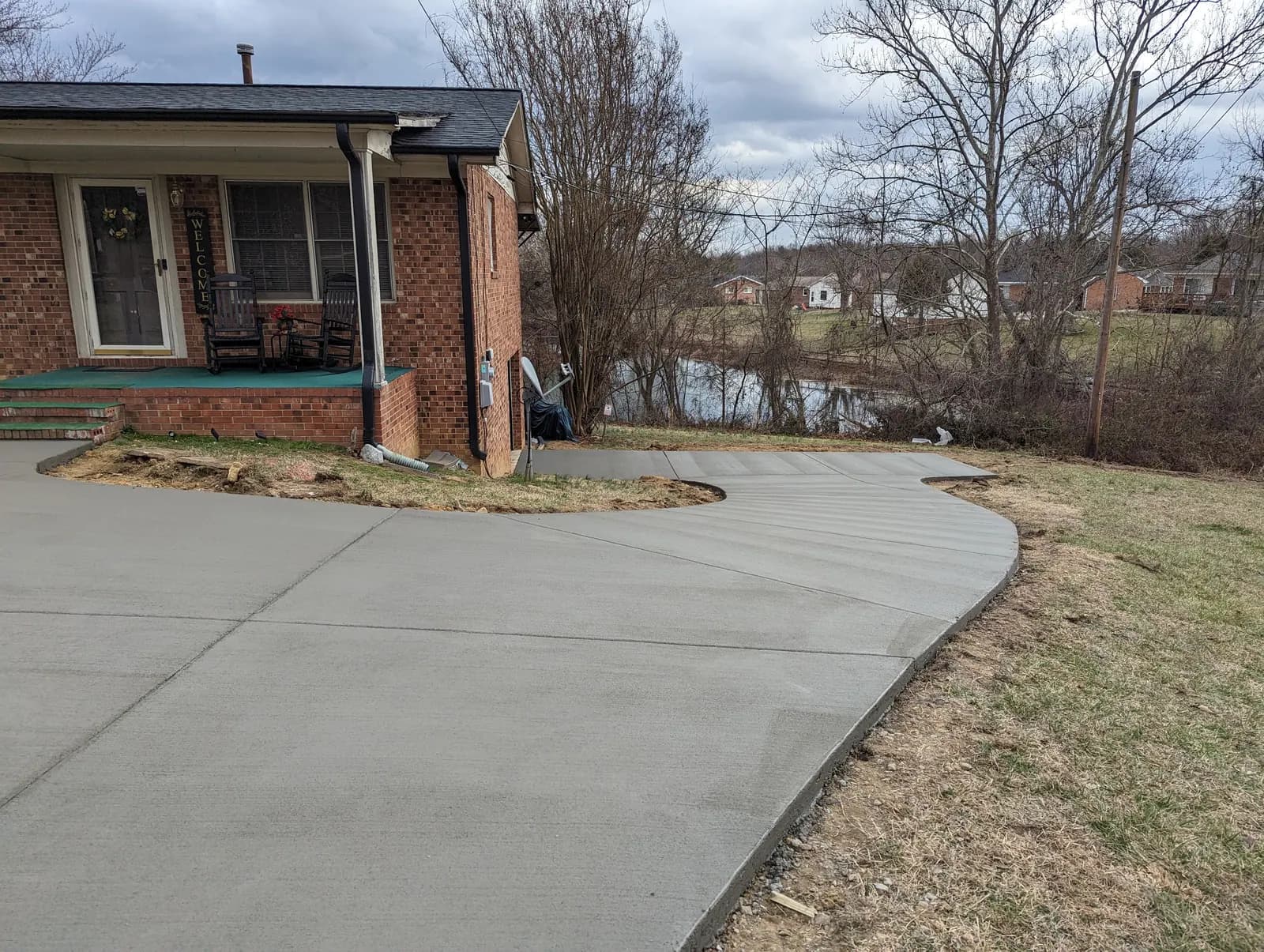Broom-finished replacement driveway with flared apron at a brick home