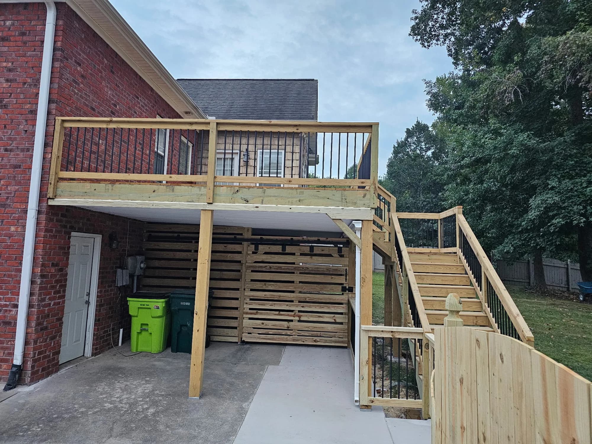 Completed elevated wood deck with stairs, black balusters, and privacy screening