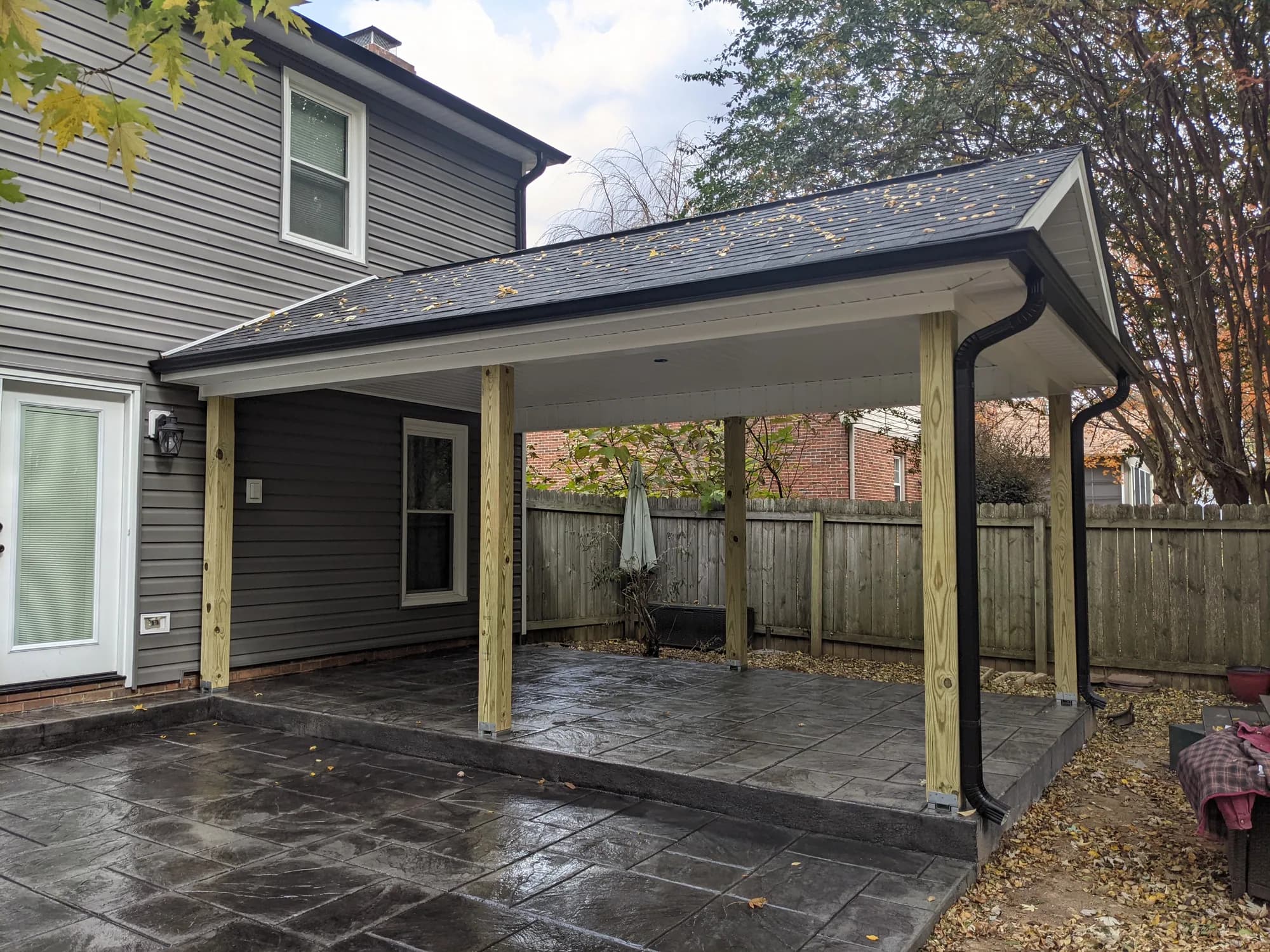 Roofed patio cover with wood posts over dark stamped concrete