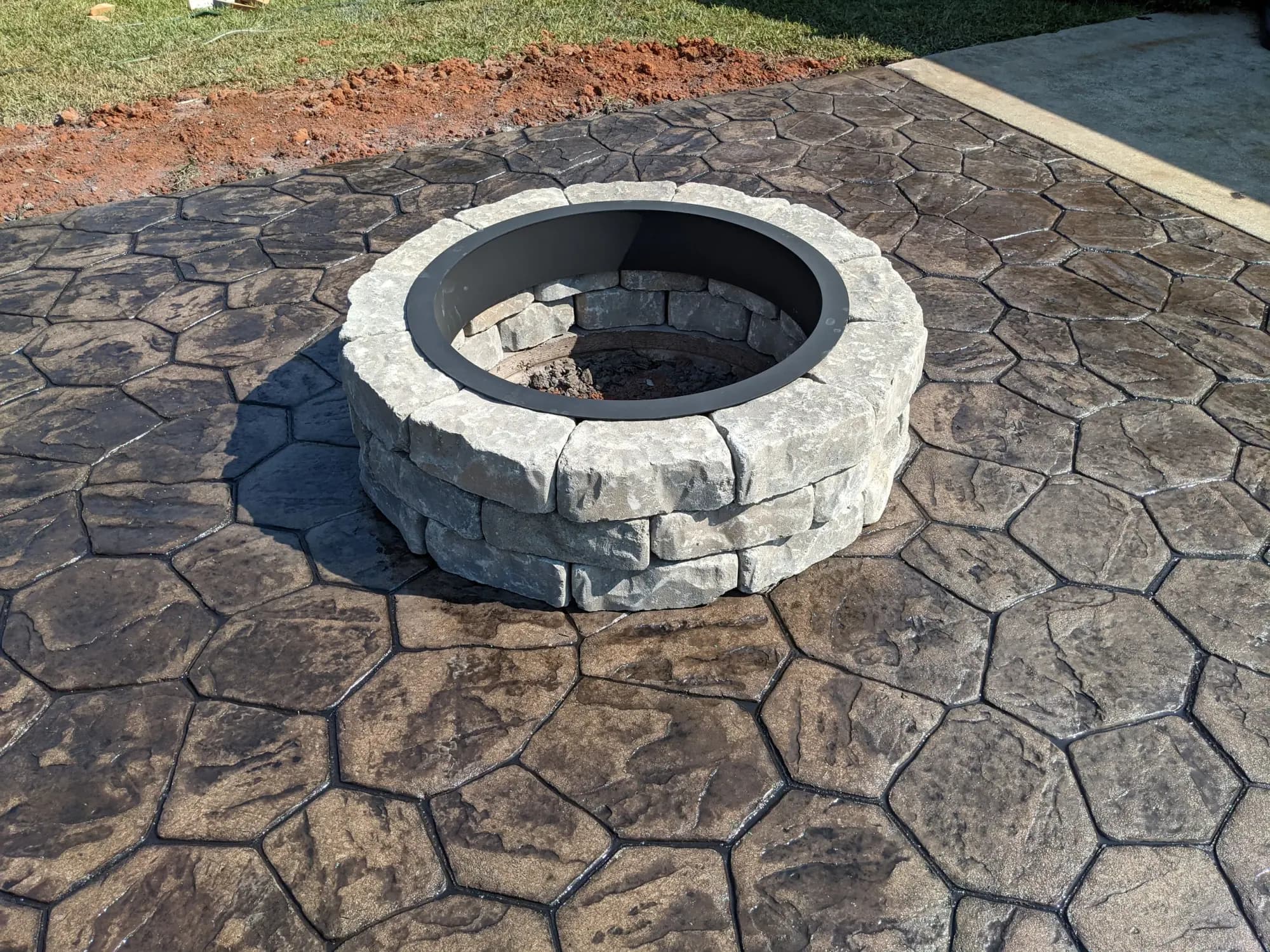 Random stone stamped concrete patio with a steel fire ring in sand with dark gray release, Bethania, NC